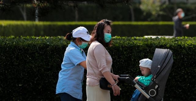 Två kvinnor promenerar med ett barn i Peking.  Andy Wong / TT NYHETSBYRÅN