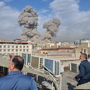 Människor i Teheran ser på när rökmolnen stiger över staden.