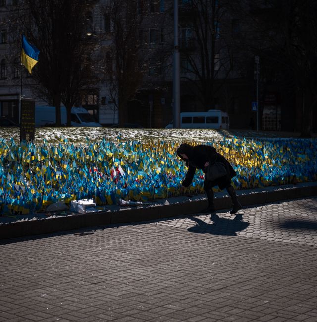 A woman places a Ukrainian flag at a memorial for those killed during the war, near Maidan Square in central Kyiv, Ukraine, Sunday, Feb. 12, 2023.  Emilio Morenatti / AP