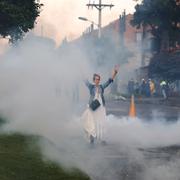 En kvinna höjer sina armar i tårgasmolnen vid sammandrabbningar mellan demonstranter och polis i Bogota i helgen