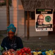 En kvinna säljer frukt och grönsaker utanför en vallokal. I bakgrunden hänger en valaffisch med Jacob Zuma på. 