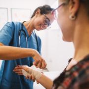 Professional nurse at the hospital bandaging the hand with a medical bandage for a woman patient.