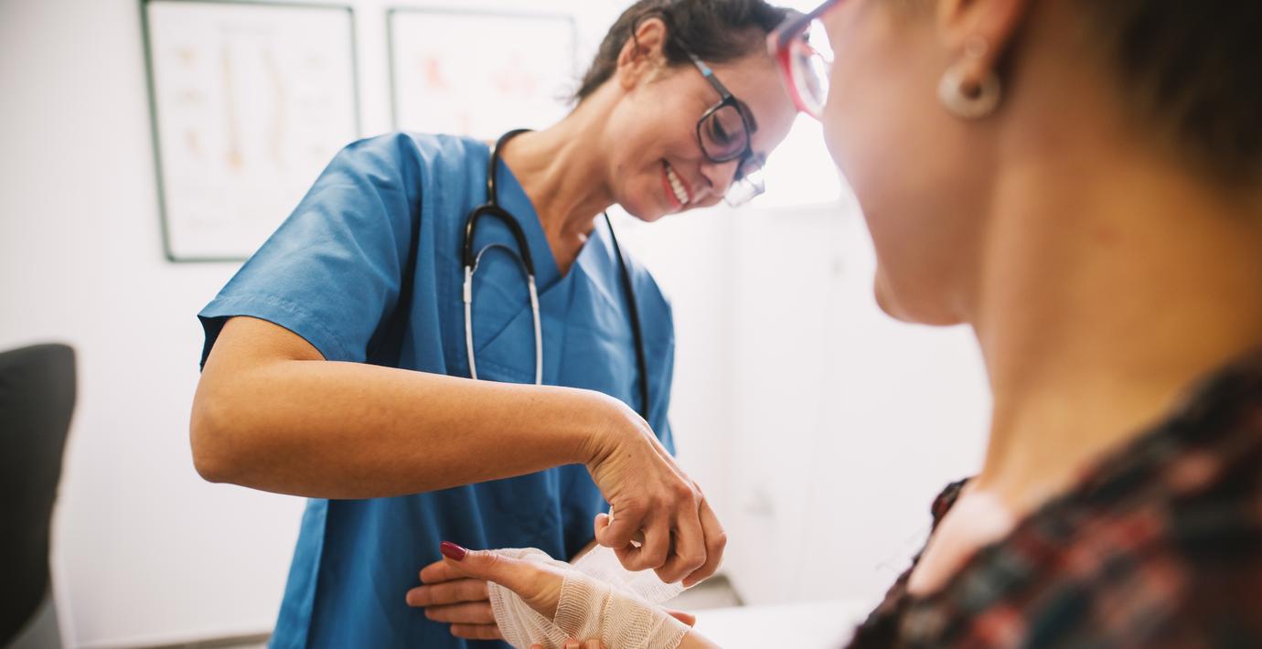 Professional nurse at the hospital bandaging the hand with a medical bandage for a woman patient.