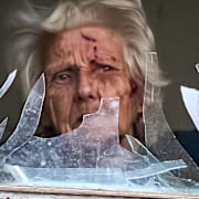 En kvinna tittar ut genom sitt förstörda fönster efter en drönarattack mot Kyiv dagen före julafton.