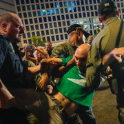 En man grips i Tel Aviv. Till höger tänder demonstranter fyrverkerier. 