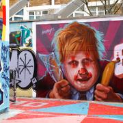 En man fotograferar en graffitivägg föreställande Boris Johnson. 