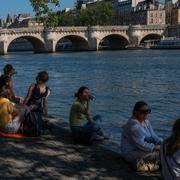 Människor sitter i skuggan längsmed floden Seine i Paris.  Michel Euler / AP