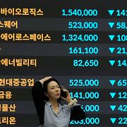 En anställd talar i telefon framför en skärm med fallande aktiekurser på Korea Exchange i Seoul.