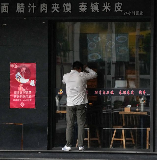A man peeps into a shuttered restaurant near locked-down communities on Wednesday, April 27, 2022, in Beijing.  Andy Wong / AP