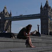 En kvinna sitter framför Tower Bridge i London.