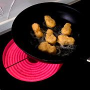 Arkivbild med stekpanna med chicken nuggets på en röd och het spisplatta.