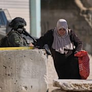 En palestinsk kvinna bär sina ägodelar förbi israeliska soldater på västbanken, i samband med rivningen av ett flyktingläger tidigare i december.