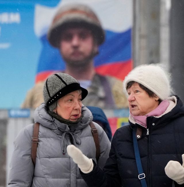 Women talk walking past a billboard with a portrait of a Russian soldier awarded for action in Ukraine and the words "Glory to the heroes of Russia" in St. Petersburg, Russia, Tuesday, Jan. 31, 2023. (AP Photo/Dmitri Lovetsky)  XDL102 Dmitri Lovetsky / AP