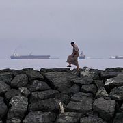 En man går på klippor vid kusten i Khor Fakkan i Förenade arabemiraten medan olje- och lastfartyg ligger uppradade i Hormuzsundet. Bilden är tagen den 11 mars 2026.