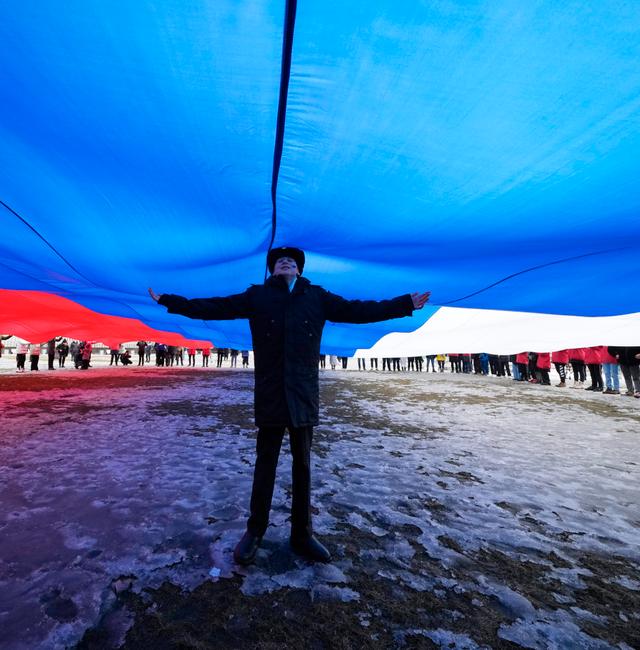 A Navy school cadet stands under a giant Russian flag during an action to mark the ninth anniversary of the Crimea annexation from Ukraine, in St. Petersburg, Russia, Saturday, March 18, 2023.  Dmitri Lovetsky / AP