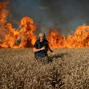 Fotojournalisten Evgeniy Maloletka  flyr från elden i ett brinnande vetefält några få kilometer från den ukrainsk-ryska gränsen. Vetefälten tros ha fattat eld efter att ha träffats av ryskt artilleri i slutet på juli förra året. 