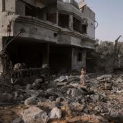 Palestinsk flicka framför en förstörd byggnad.