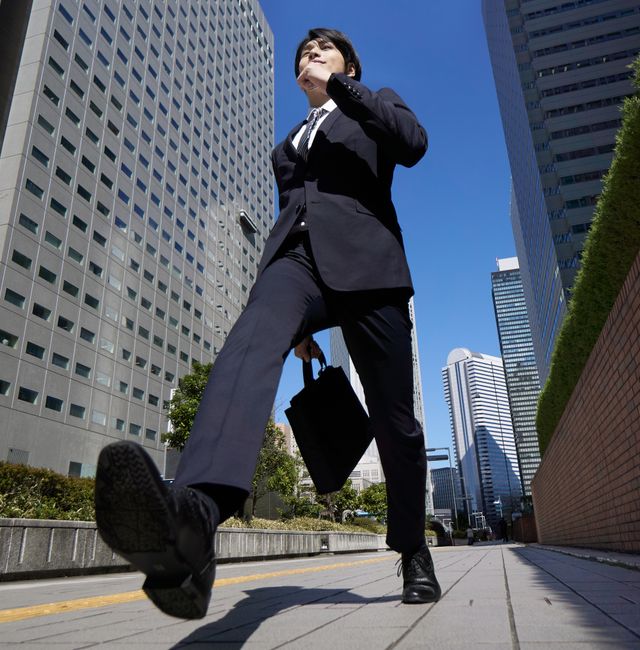 A Japanese male businessman walks briskly through an office district. Shutterstock