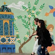 Två kvinnor passerar en muralmålning i Teheran. 