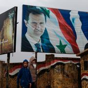 Två personer framför en affisch på Syriens president Bashar al-Assad och Rysslands dito Vladimir Putin.