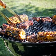 En person grillar kött och majskolvar.