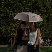 Två kvinnor använder ett paraply för att skydda sig från solen under en promenad i Paris i juli.