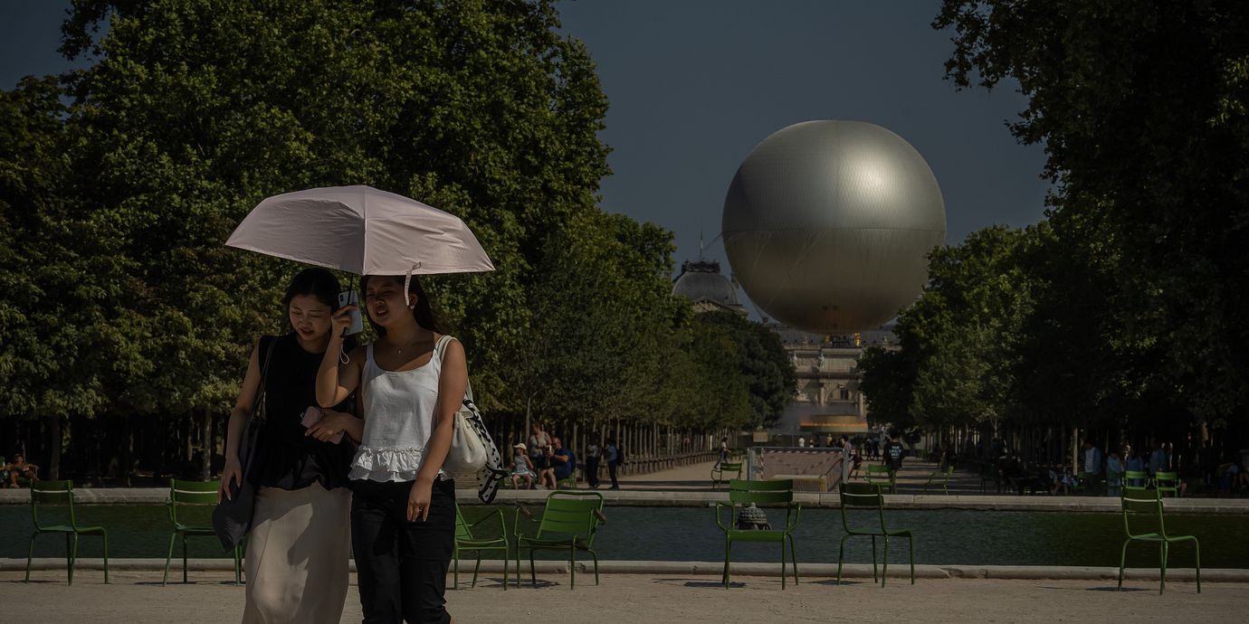 Två kvinnor använder ett paraply för att skydda sig från solen under en promenad i Paris i juli.