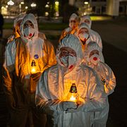 Människor iklädda skyddsdräkter tänder ljus för att minnas offren för kärnkraftsolyckan. Bild från Ukraina.